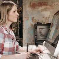 AkZ_BP_08_2026 | akz-media.de Woman in a plaid shirt working at a large desktop computer on a studio desk with a stylus nearby?