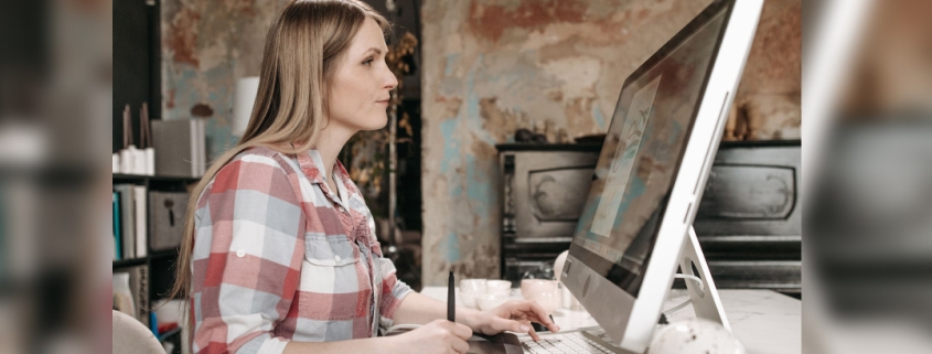 AkZ_BP_08_2026 | akz-media.de Woman in a plaid shirt working at a large desktop computer on a studio desk with a stylus nearby?
